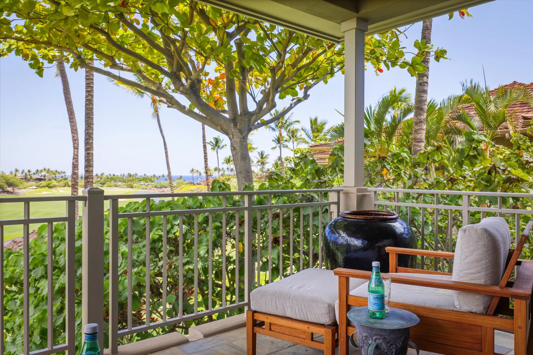 A covered outdoor seating area overlooks lush greenery and a distant ocean.