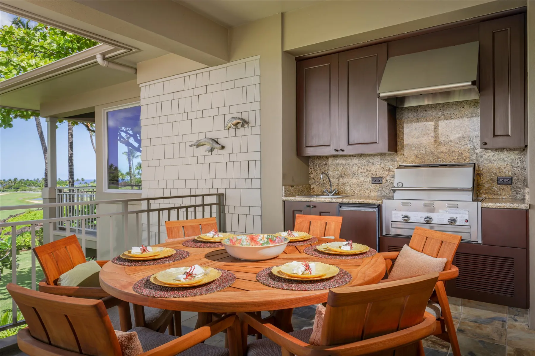 A dining area with a round table beside an outdoor kitchen and large windows.