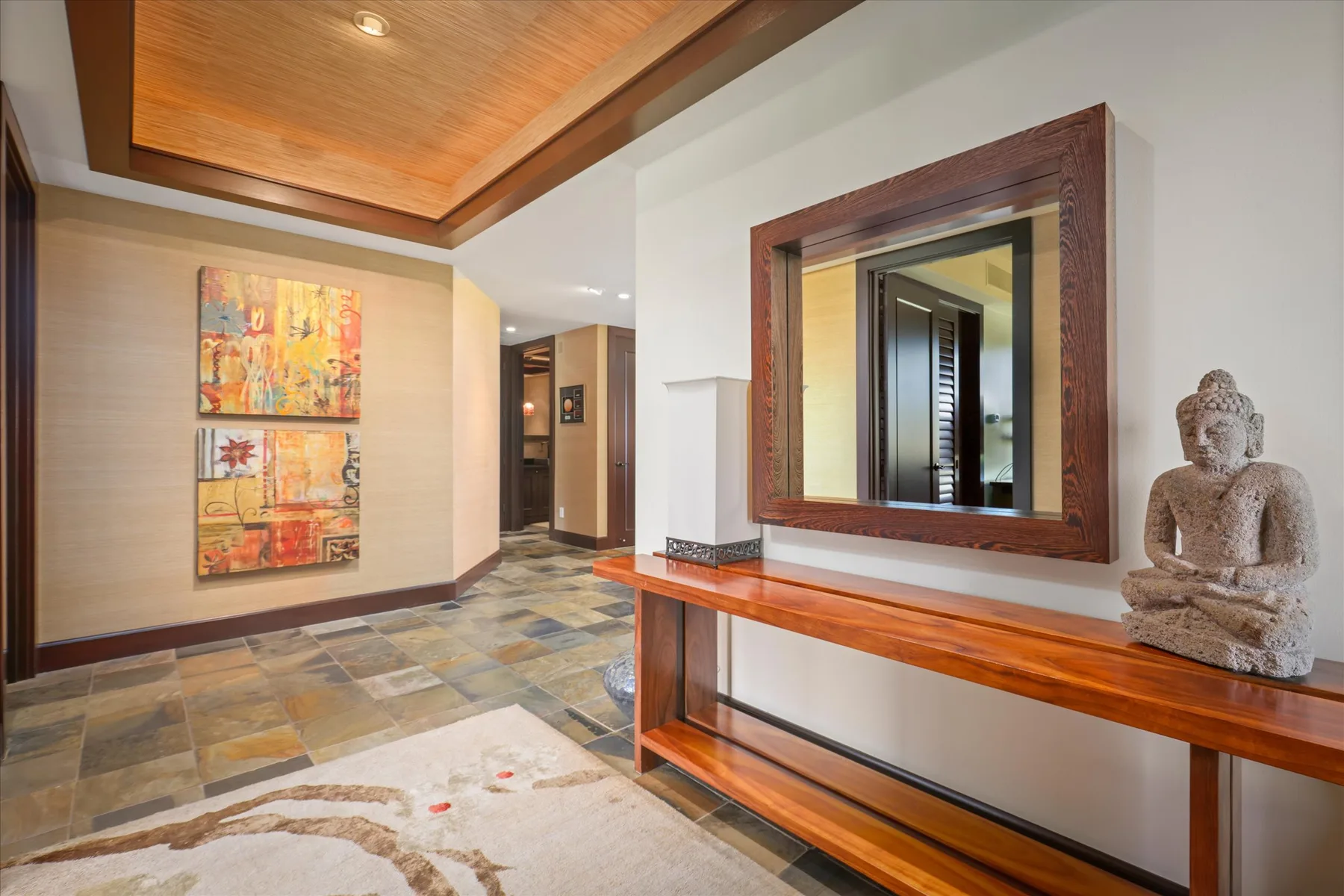 A hallway with a large wall mirror, console table, and decorative statue.