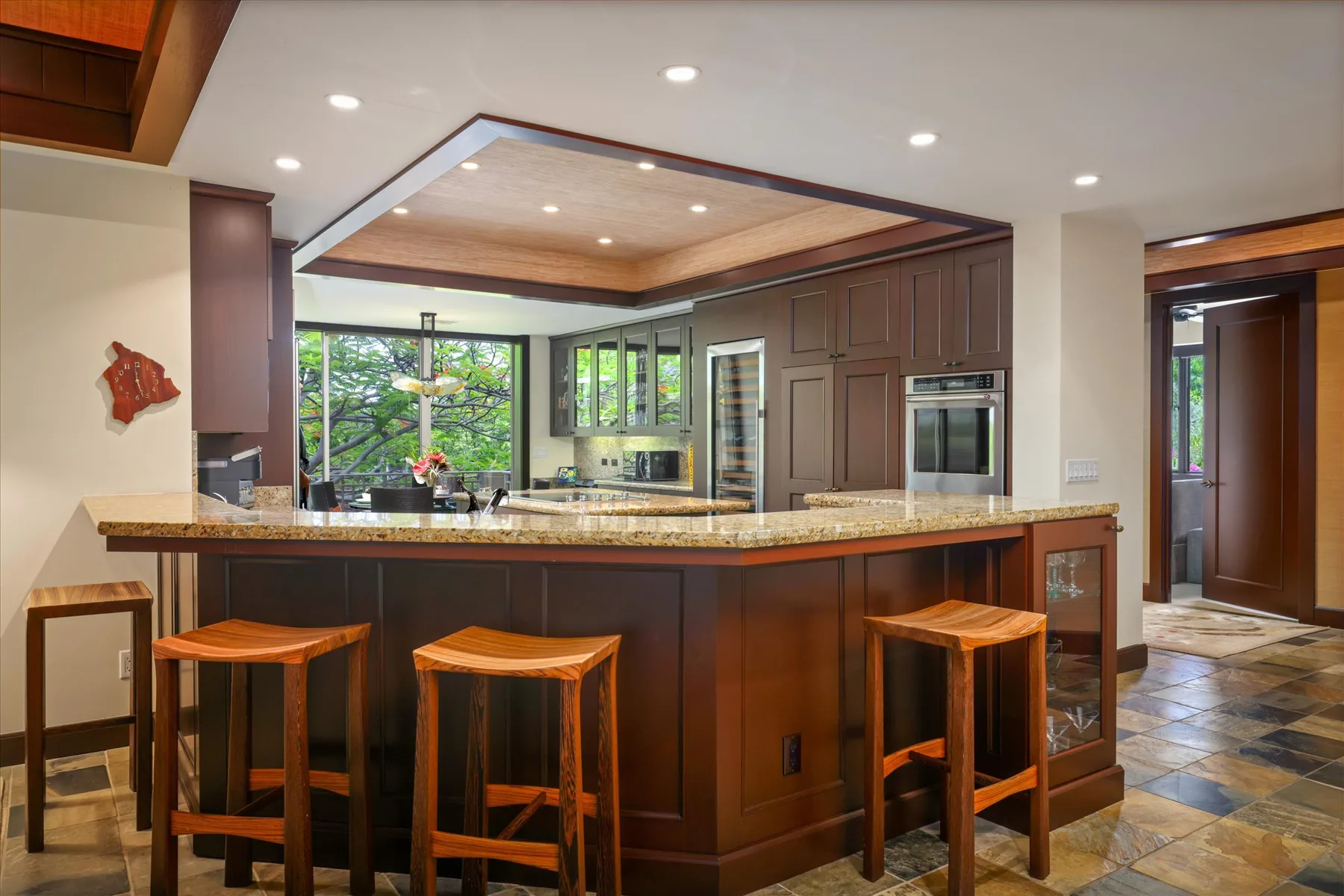 Una cocina con una isla grande, asientos de madera y gabinetes oscuros.