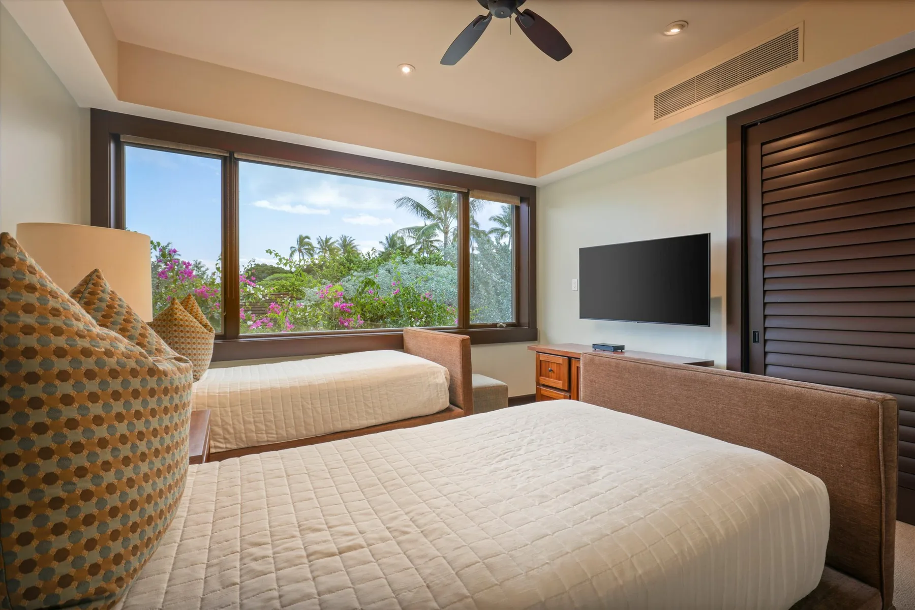 A bedroom with two beds, a large window, and a wall-mounted television.