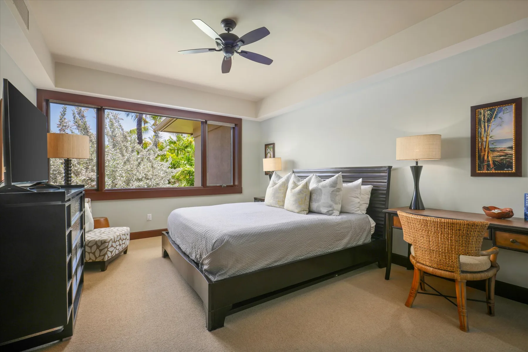 A bedroom with a large bed beside a wide window overlooking greenery.