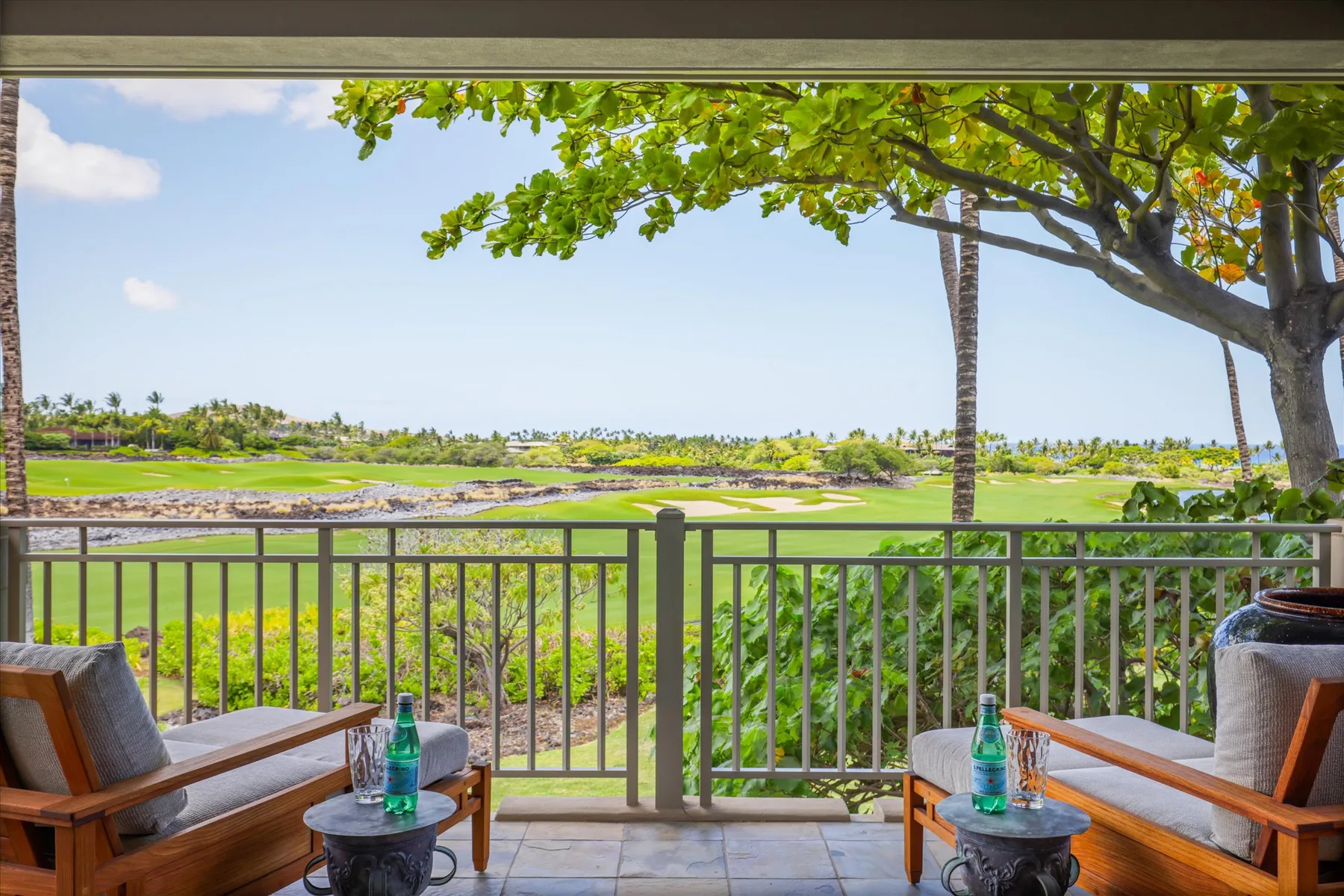 A patio seating area overlooks a green golf course beneath leafy tree branches.