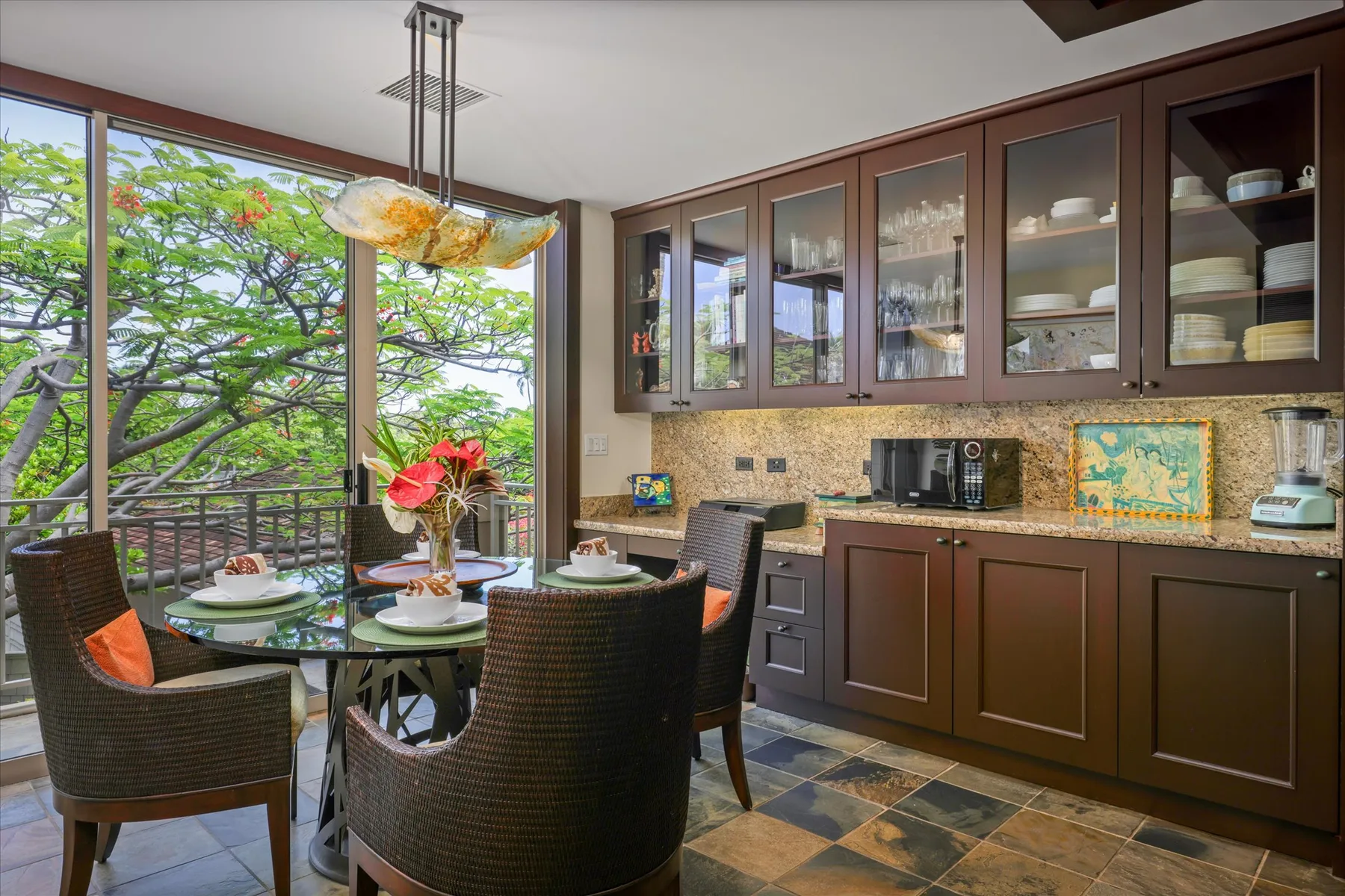 Comedor junto a una cocina, con gabinetes oscuros y ventanas con vista a los árboles.
