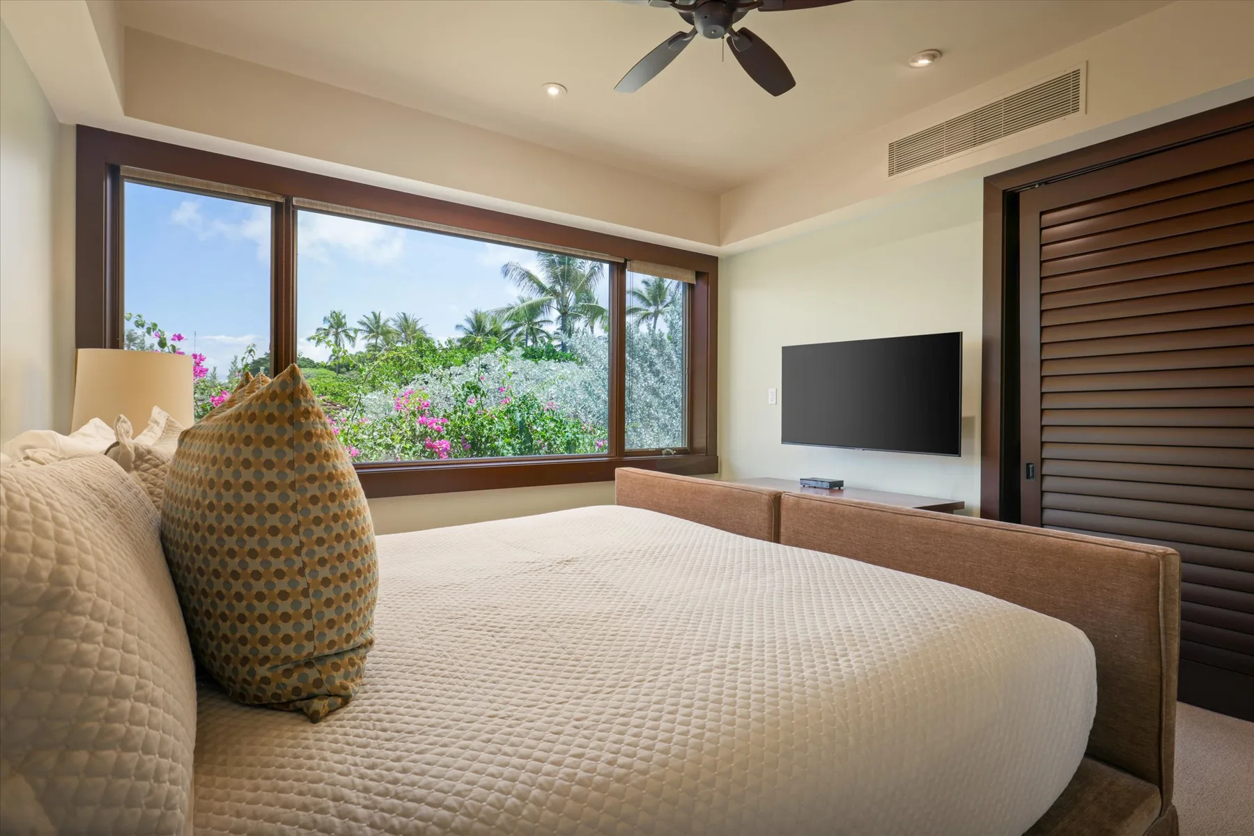 A bedroom with a large bed, wide windows, and a wall-mounted television.
