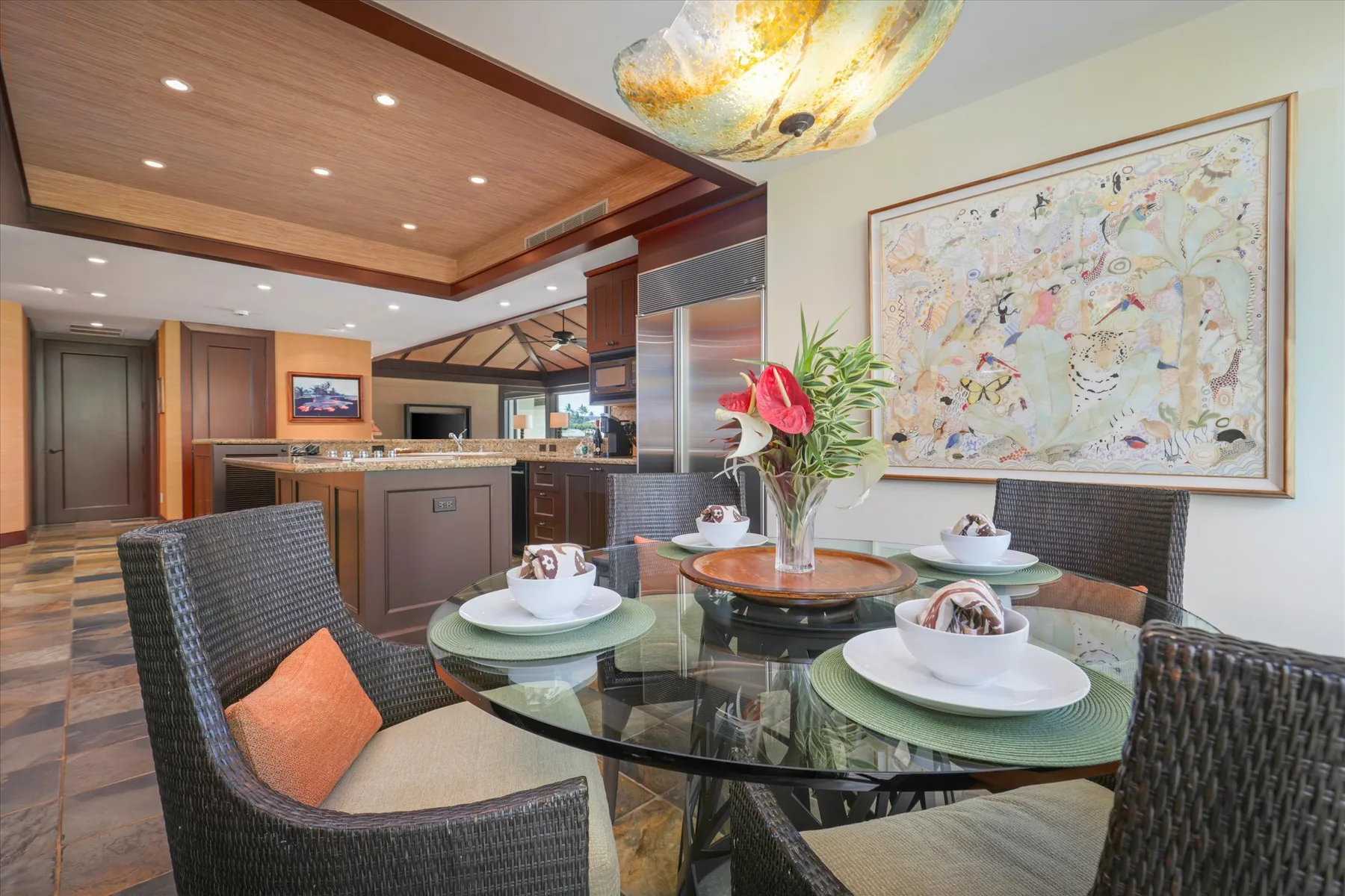 A dining area with a glass table, dark woven seating, and colorful wall art.