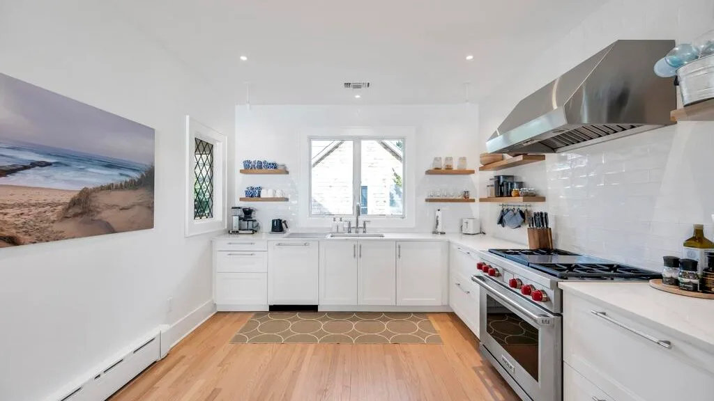 A bright kitchen with white cabinets, a central window, and a stainless steel range.