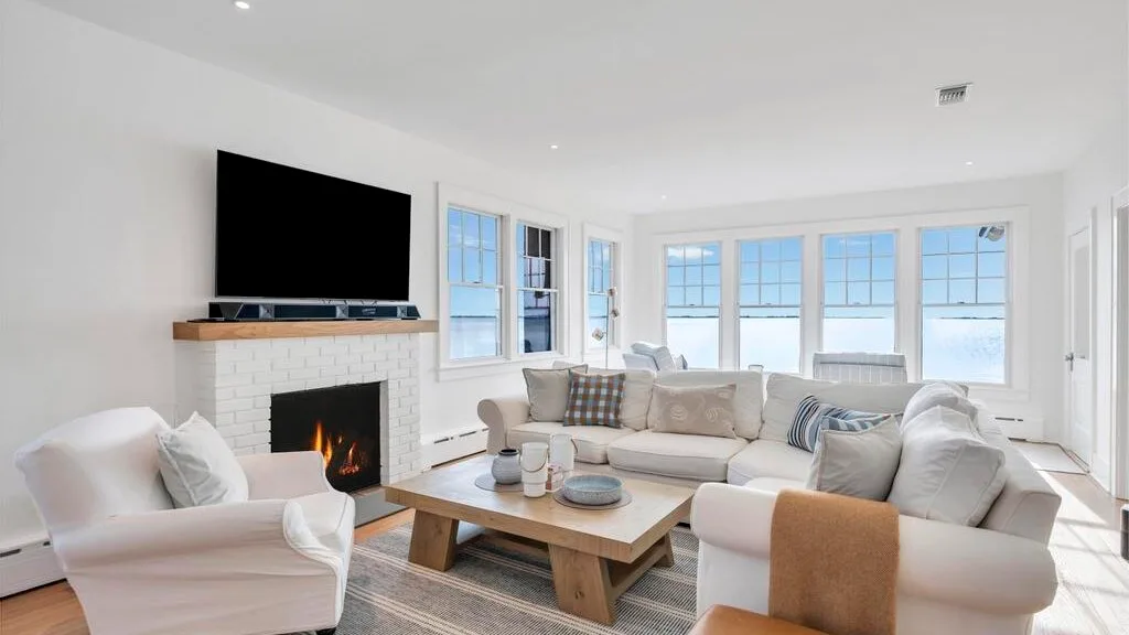 A bright living room with light seating and a television above a fireplace.