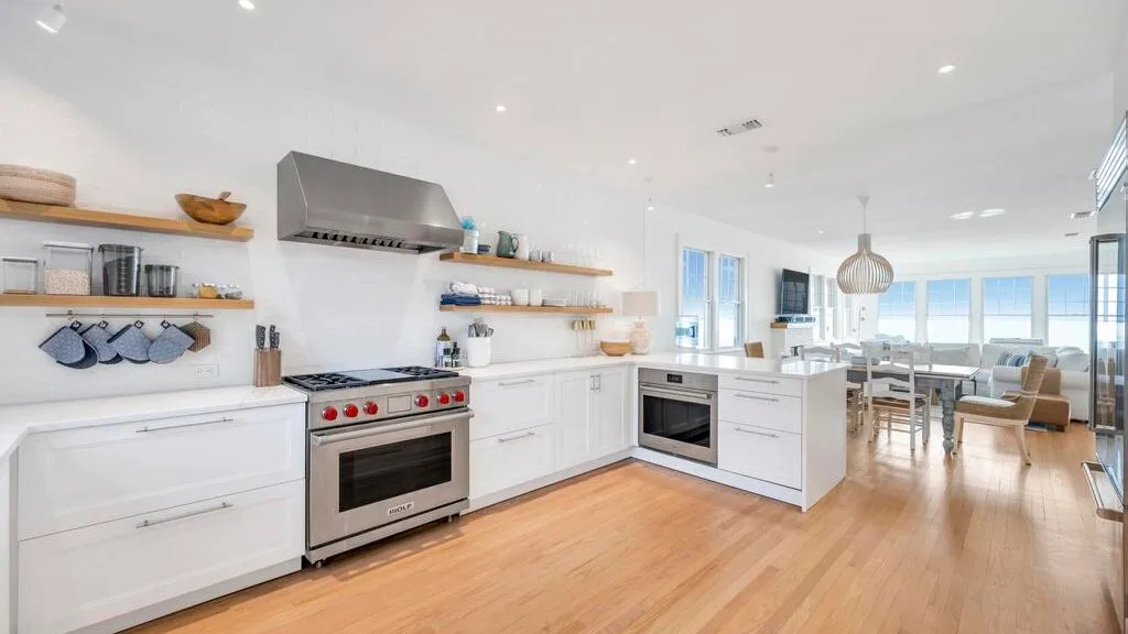 A bright open-plan kitchen and dining area with white cabinets and a wood floor.