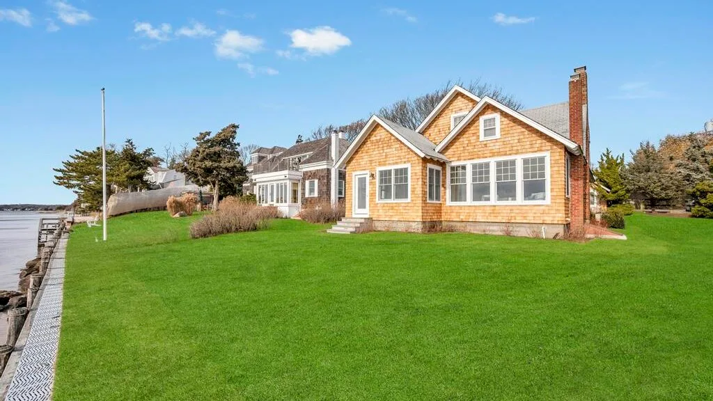 A house stands beside a broad green lawn under a clear blue sky.