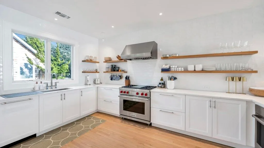 A bright white kitchen with long counters and a large window.