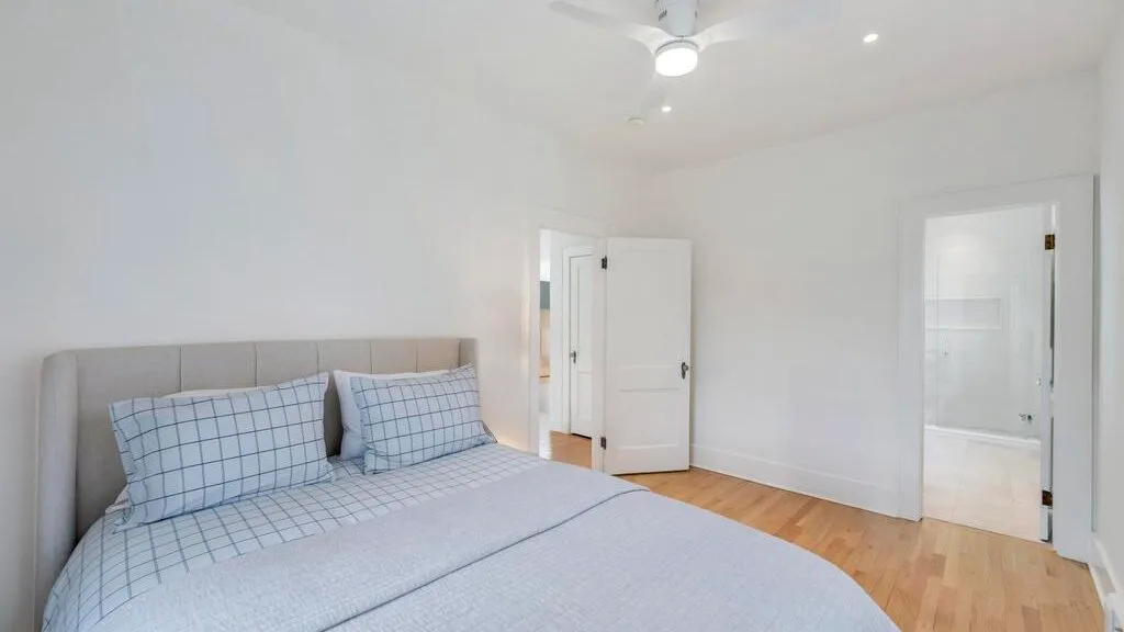 A bedroom with a bed, pale bedding, and light wood flooring.