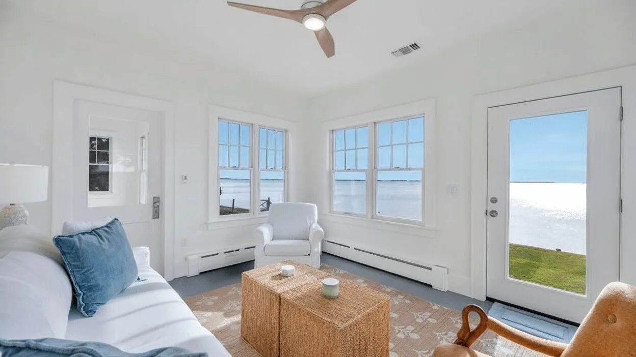 A bright living room with a seating area beside several large windows.
