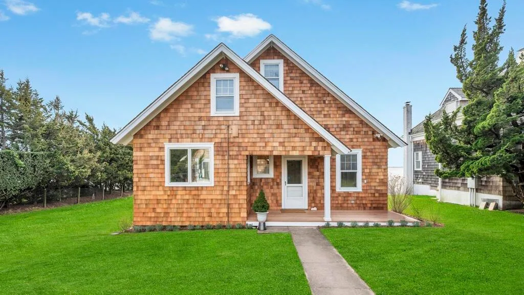 A shingled house stands beside a green lawn, with a walkway leading to the entrance.