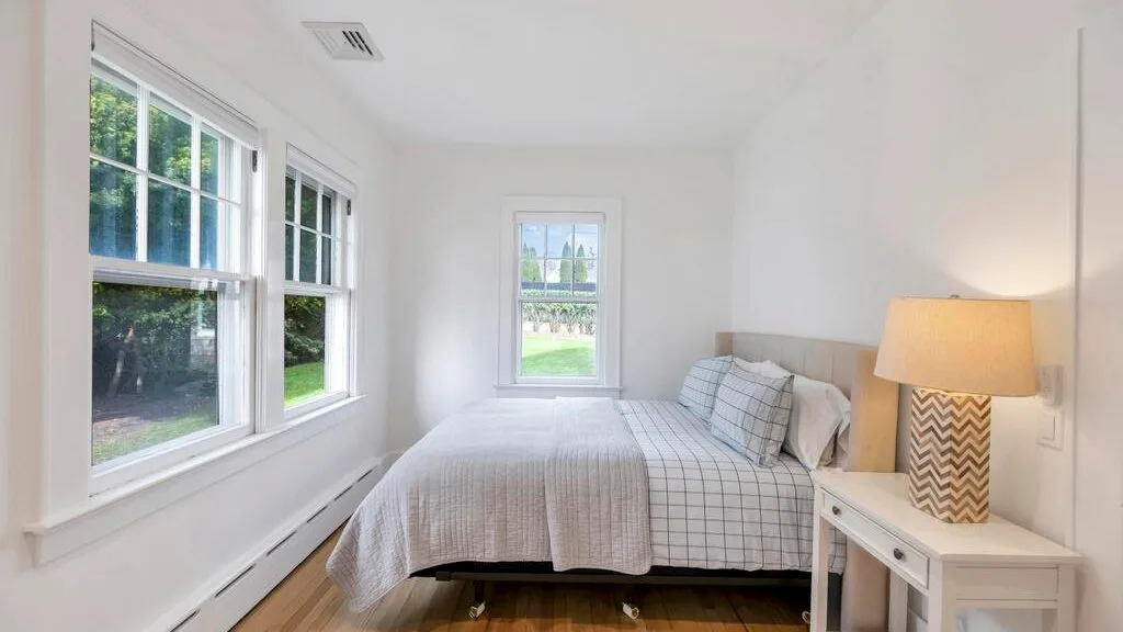 A bright bedroom with a bed beside several windows and a bedside table.