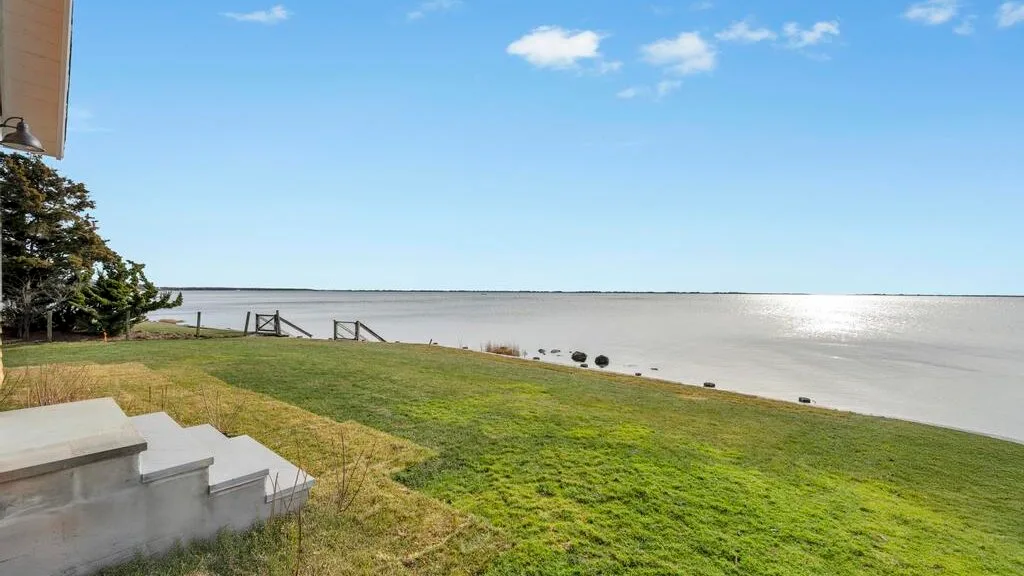 A grassy waterfront lawn slopes toward a broad body of water beneath a blue sky.