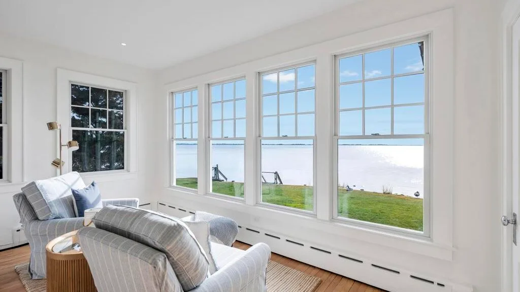 A bright living room with seating beside large windows overlooking the water.
