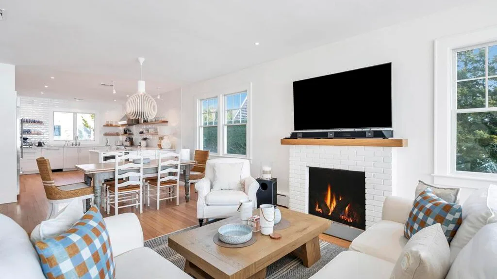 A bright open-plan living and dining area with a fireplace and large television.
