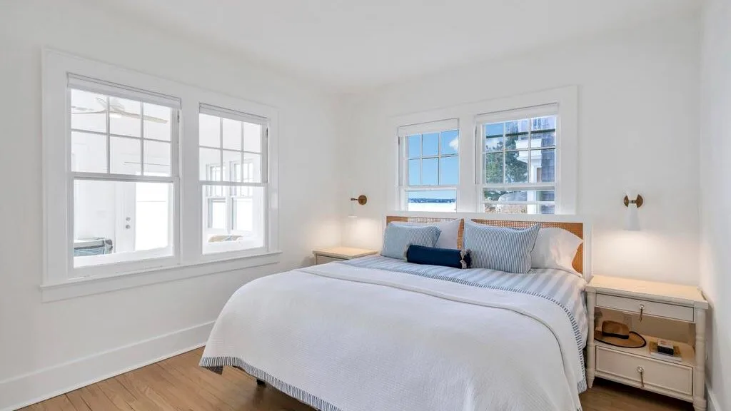 A bright bedroom with a neatly made bed and windows.