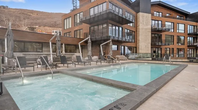 An outdoor pool sits beside a modern brick building with balconies.