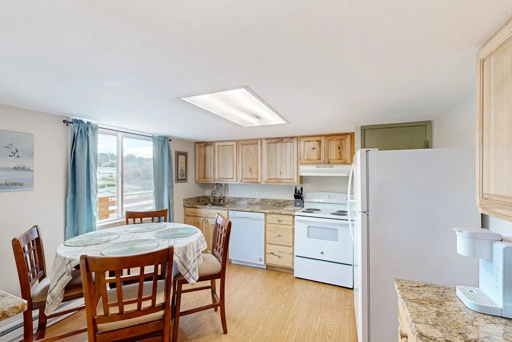 Cocina y comedor con armarios de madera y una mesa junto a la ventana.