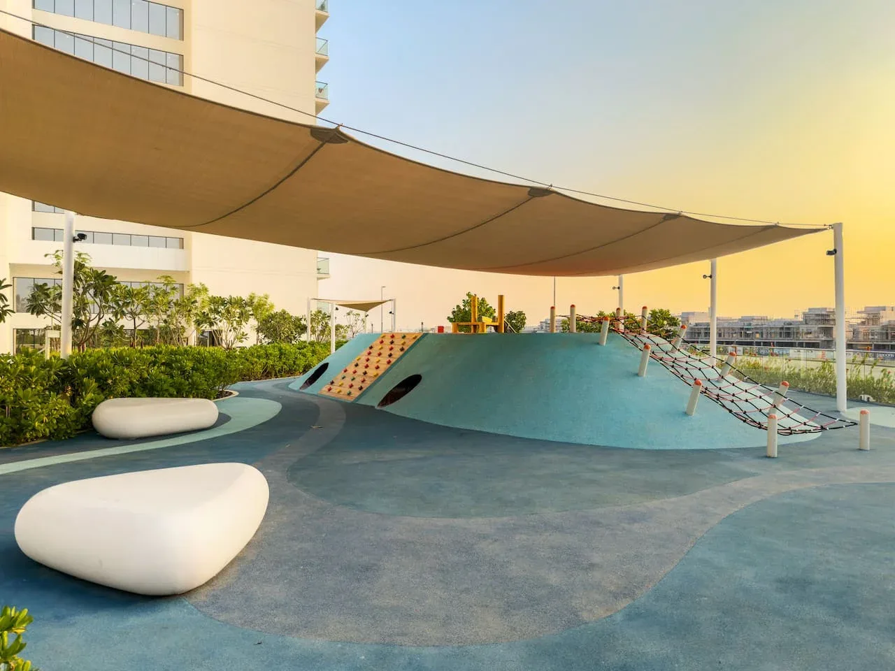 Un parque infantil al aire libre tiene un montículo bajo para trepar bajo una gran cubierta de sombra.