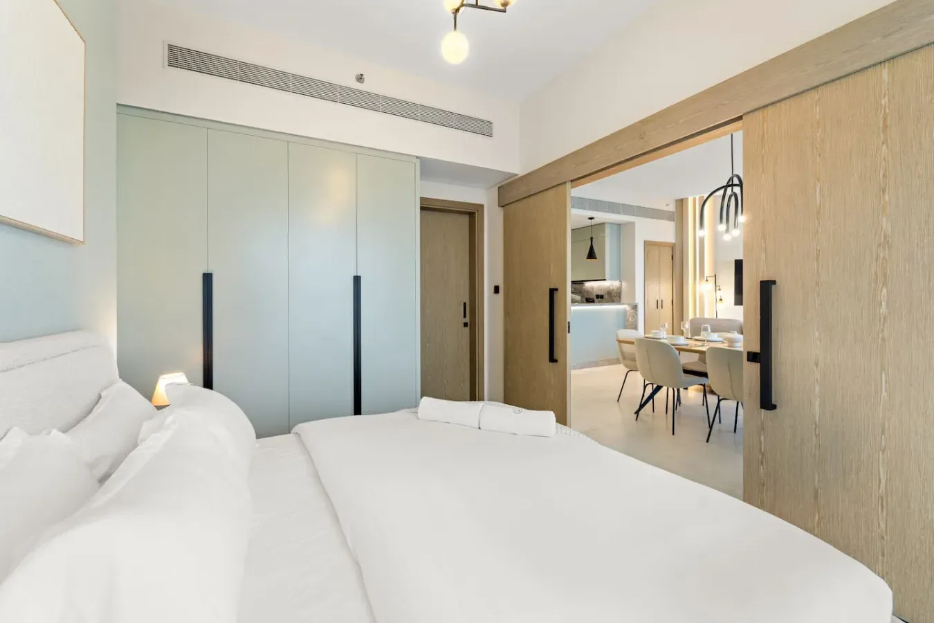 Un dormitorio con una cama blanca y puertas correderas que dan a un comedor.