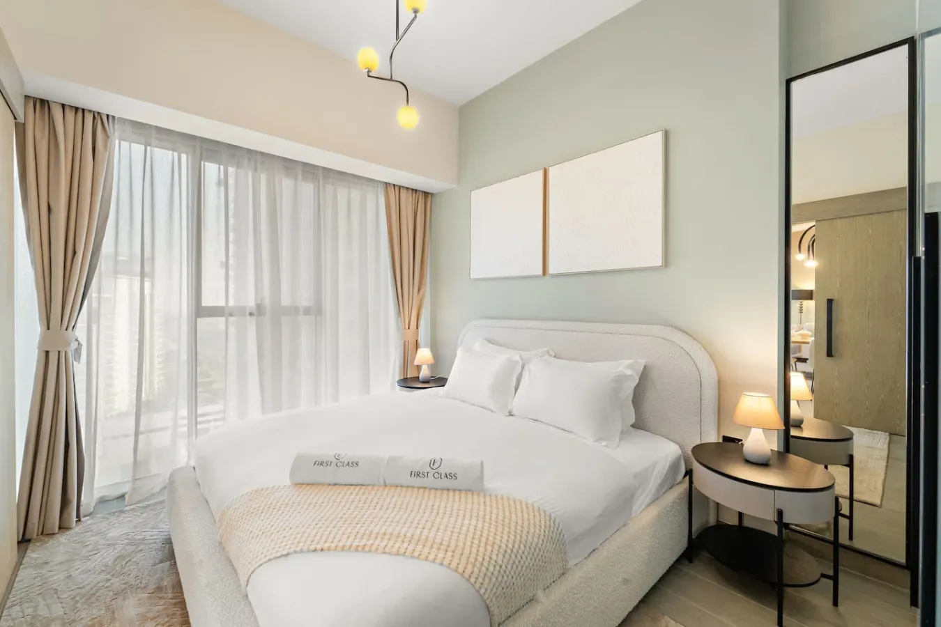 Un dormitorio luminoso con una cama blanca, mesitas de noche y una gran ventana con cortinas.