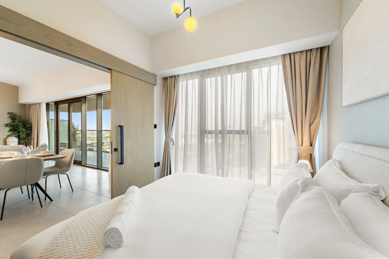 Un dormitorio luminoso con una cama blanca junto a ventanas altas con cortinas.