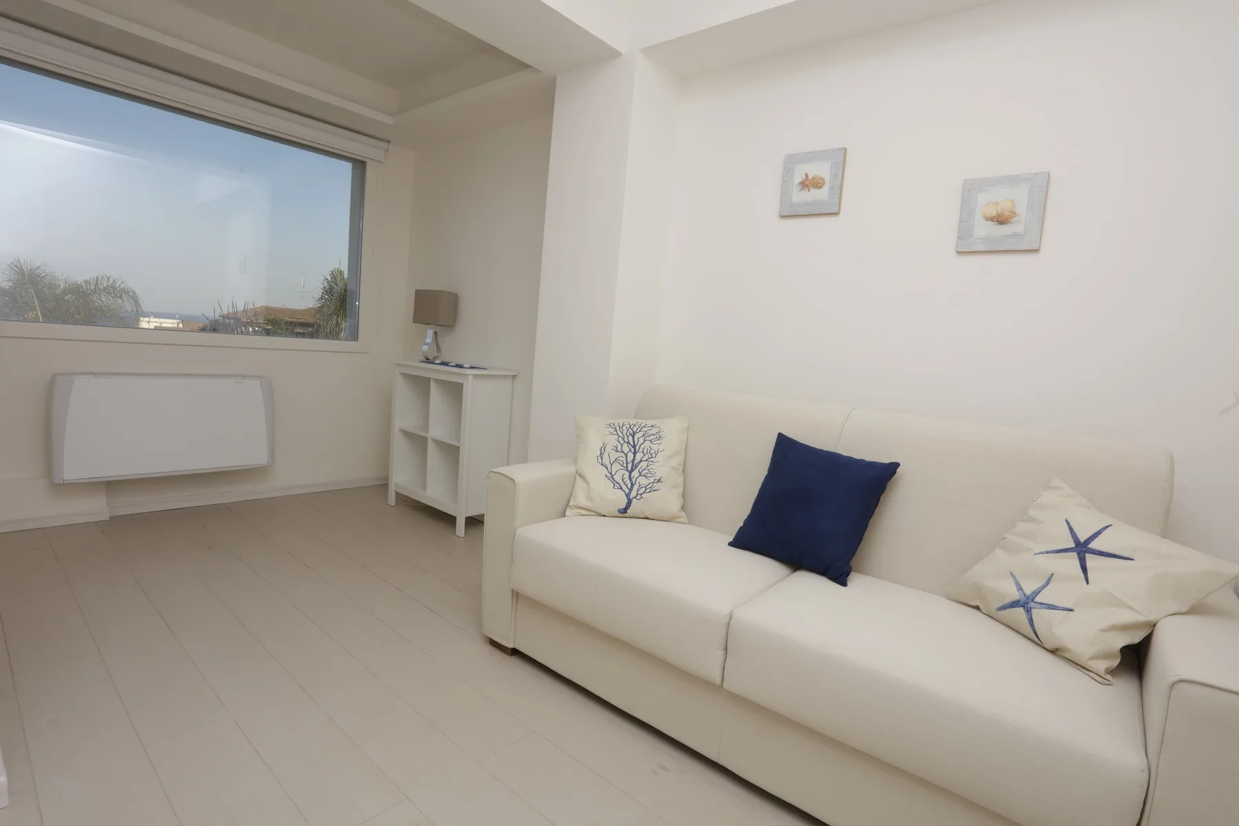 A bright living room with a white sofa beneath two small framed pictures.