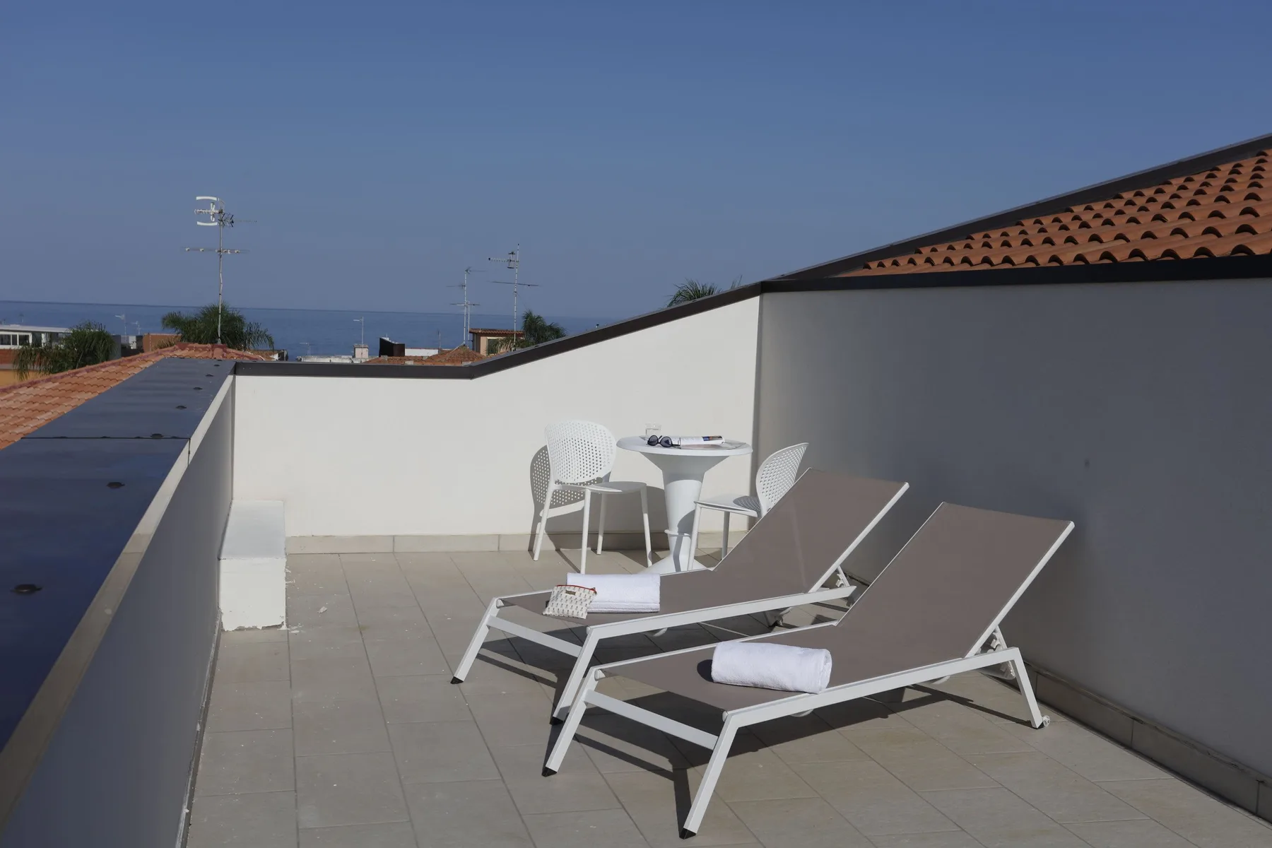 A rooftop terrace has two loungers and a small table with chairs.