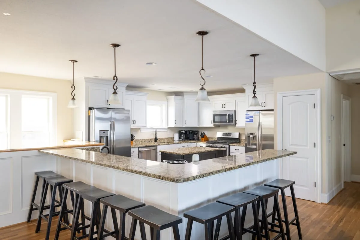 Una cocina luminosa con una isla grande, asientos y electrodomésticos de acero inoxidable.