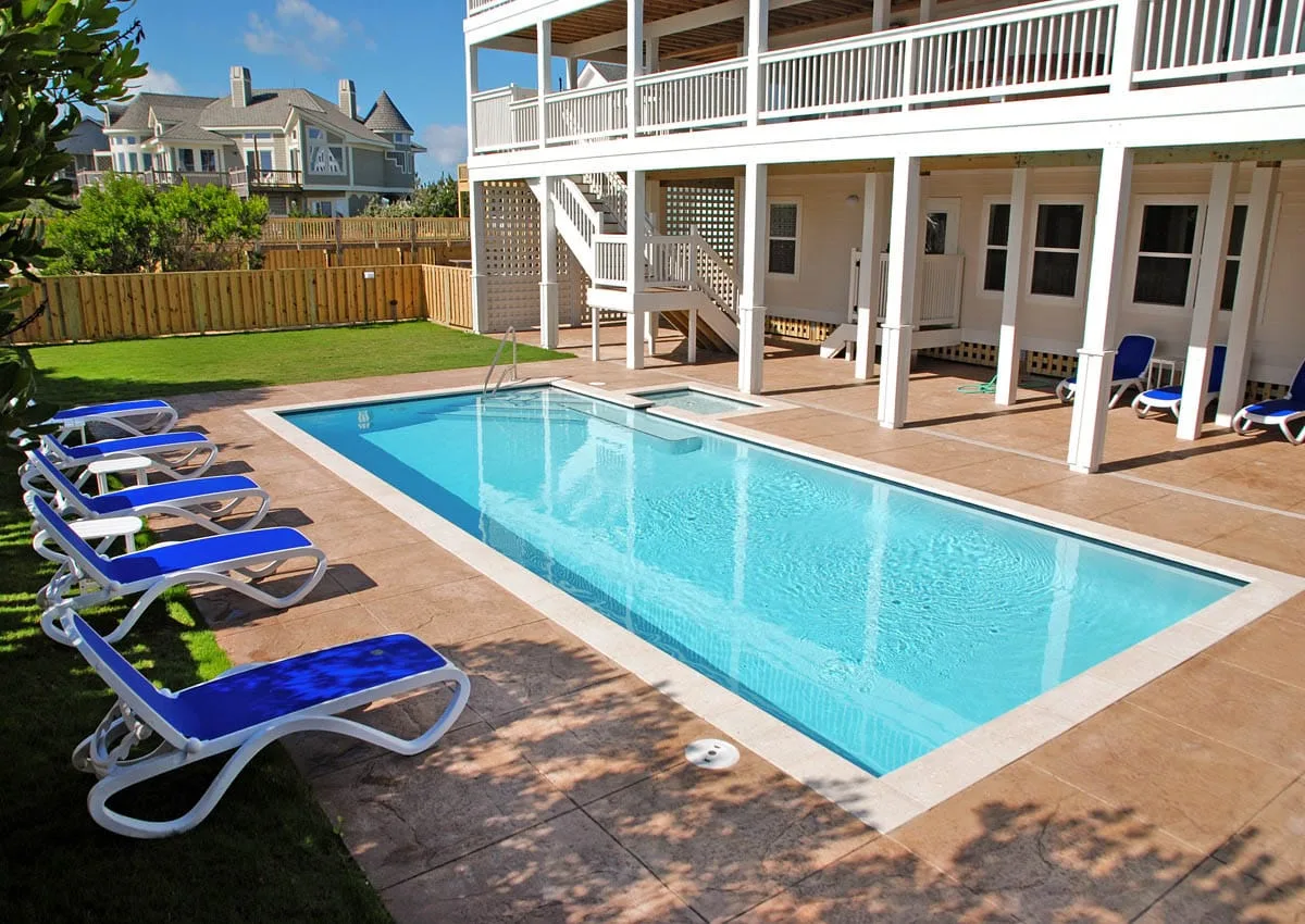 An outdoor swimming pool beside a raised white building, with lounge chairs along the deck.