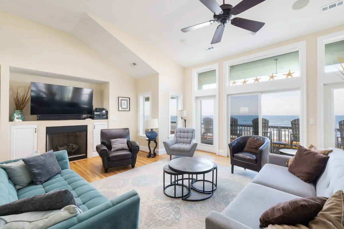A bright living room with seating, a television, and large windows overlooking the water.