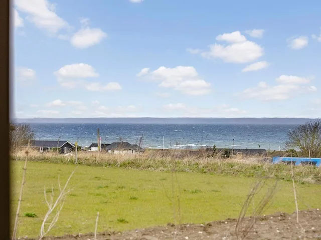 A grassy field overlooks the sea beneath a partly cloudy sky.