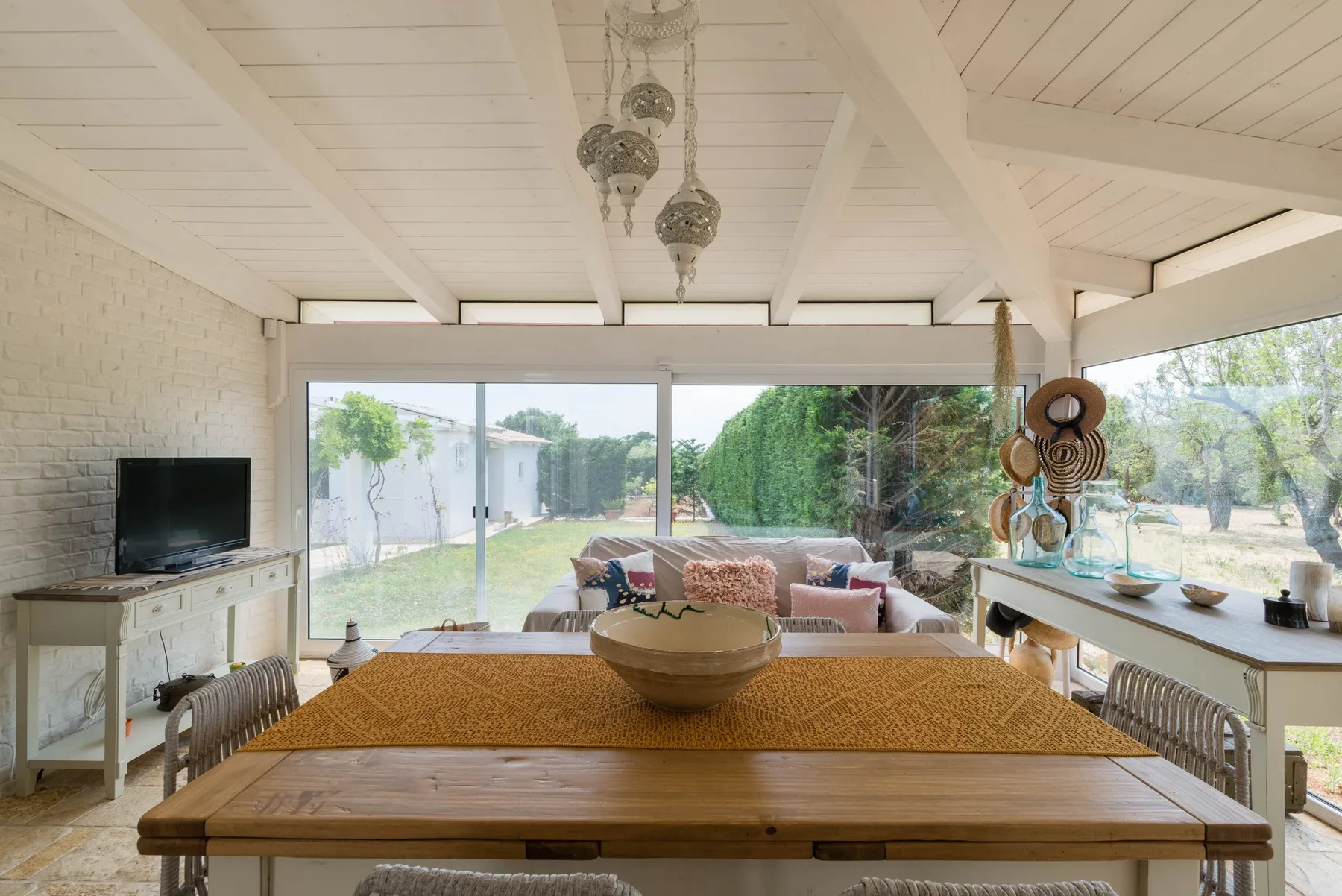 A bright living and dining area opens onto a garden through large glass windows.