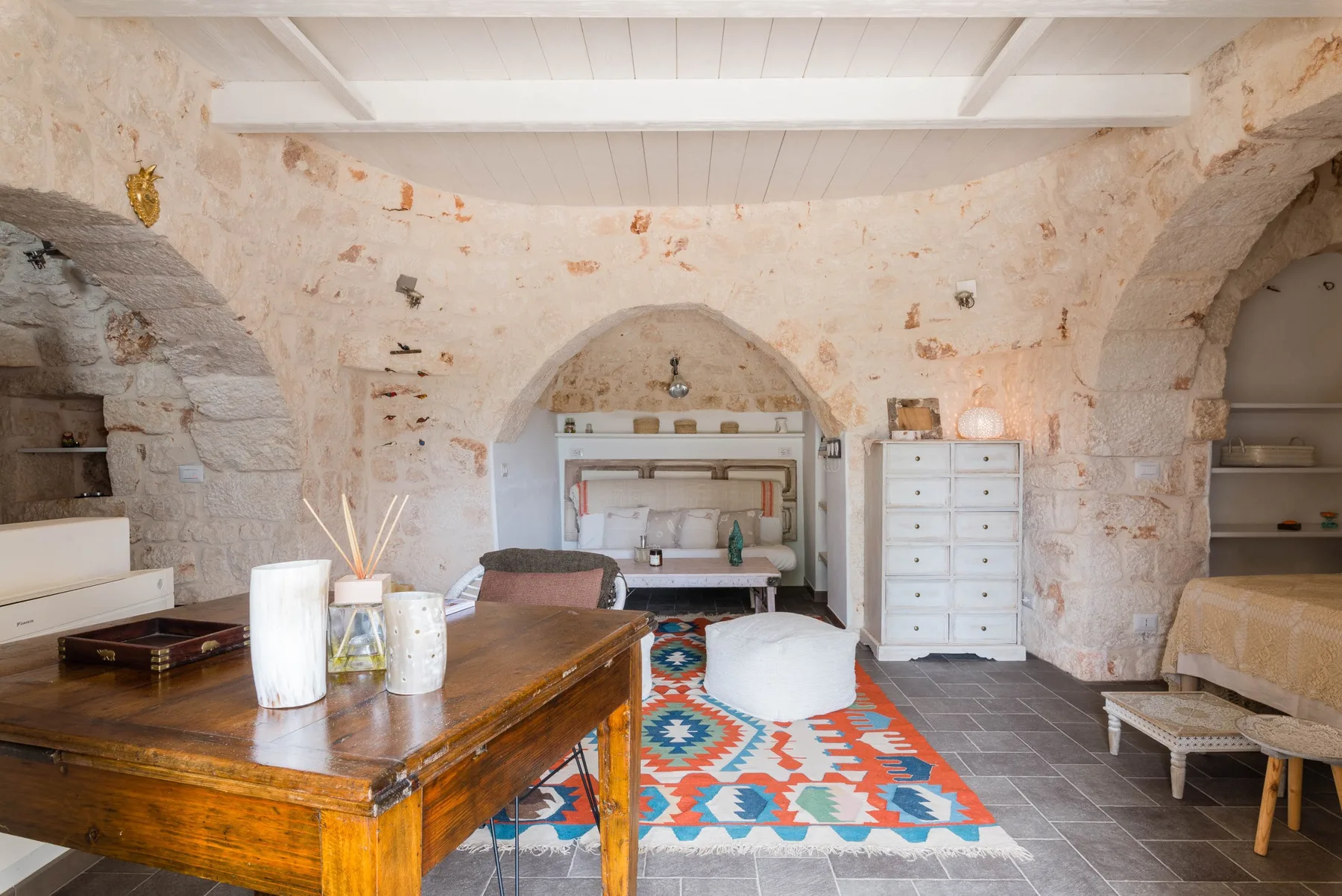 A rustic stone room with a wooden table and a colorful patterned rug.