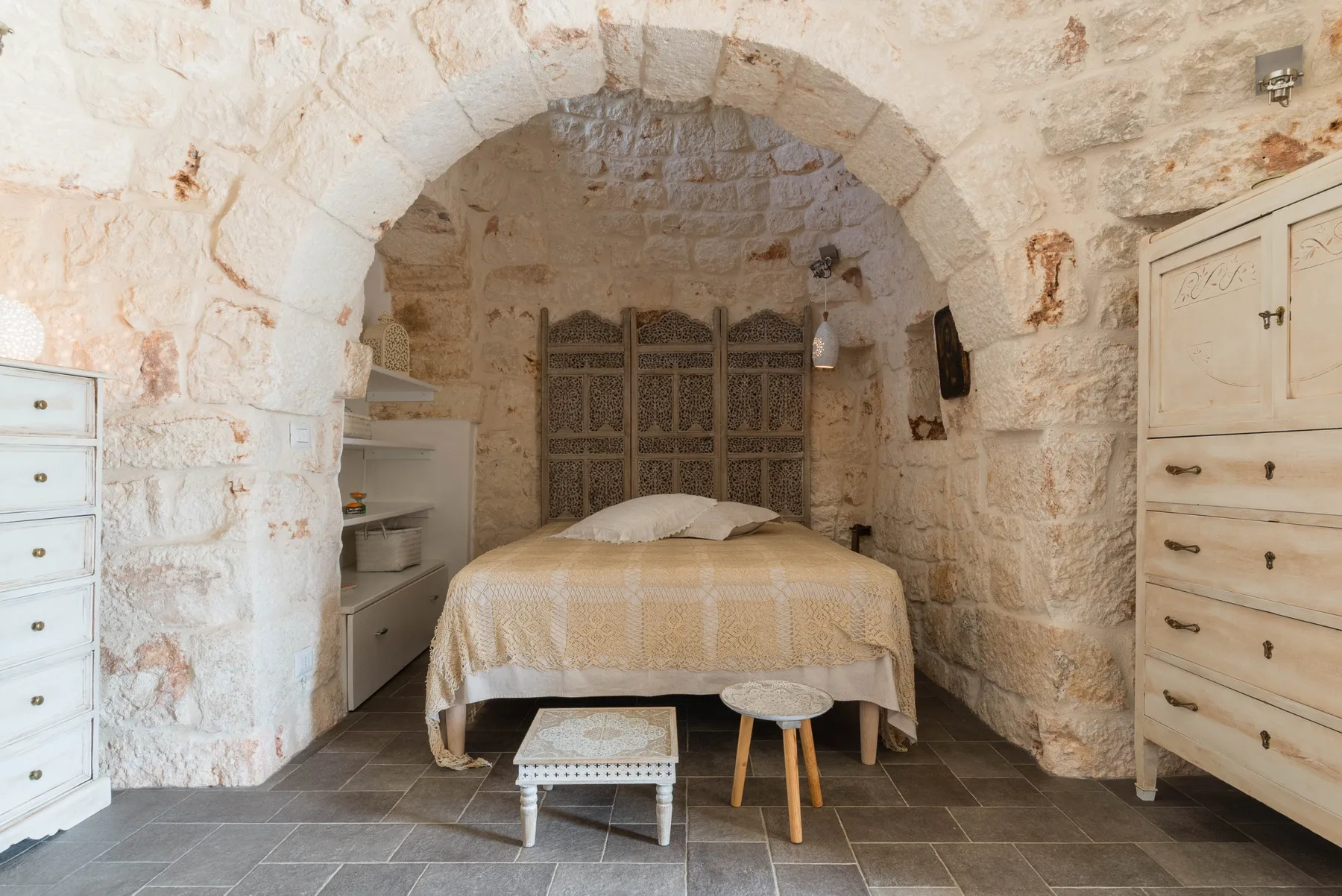 A bed sits beneath a stone arch in a bedroom, with a small table at its foot.