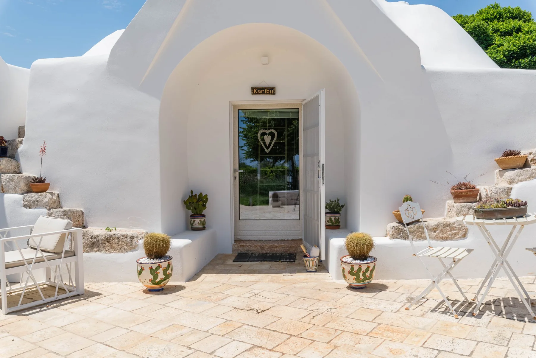 A white arched entrance opens onto a tiled patio with small tables and plants.