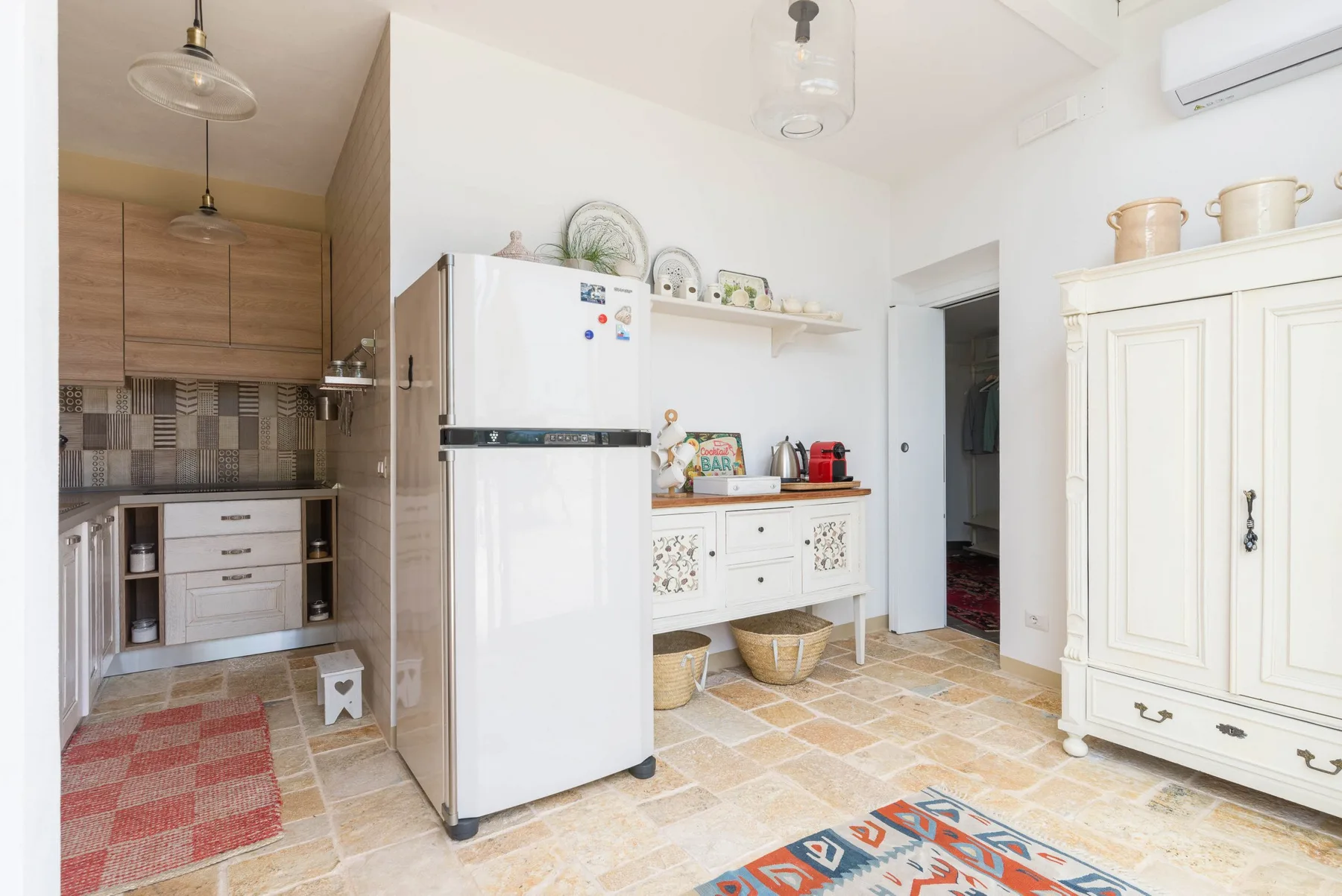 A bright kitchen with a refrigerator, cabinets, and a patterned tile floor.