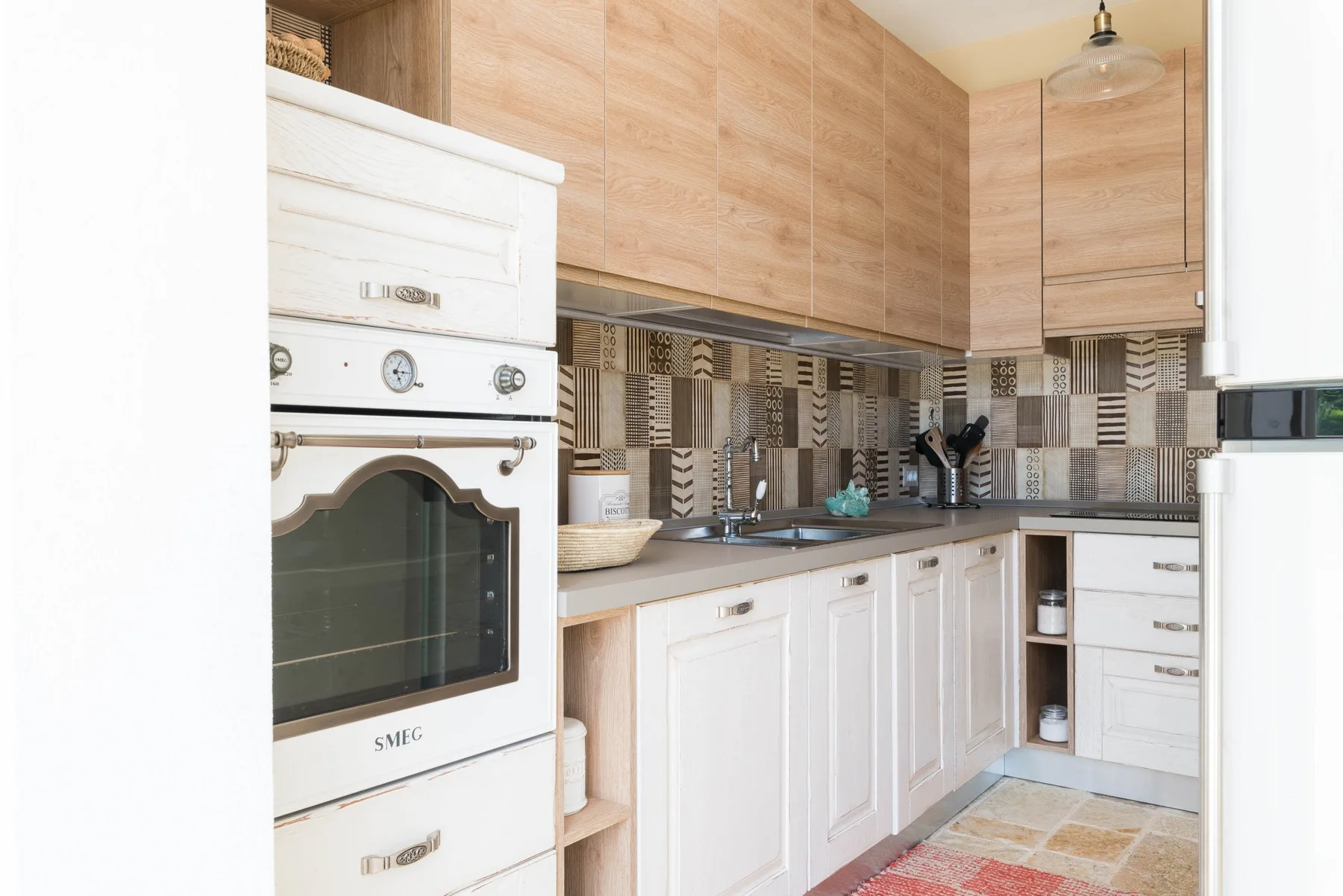 A bright kitchen with white cabinetry, wood-toned upper cabinets, and a tiled backsplash.