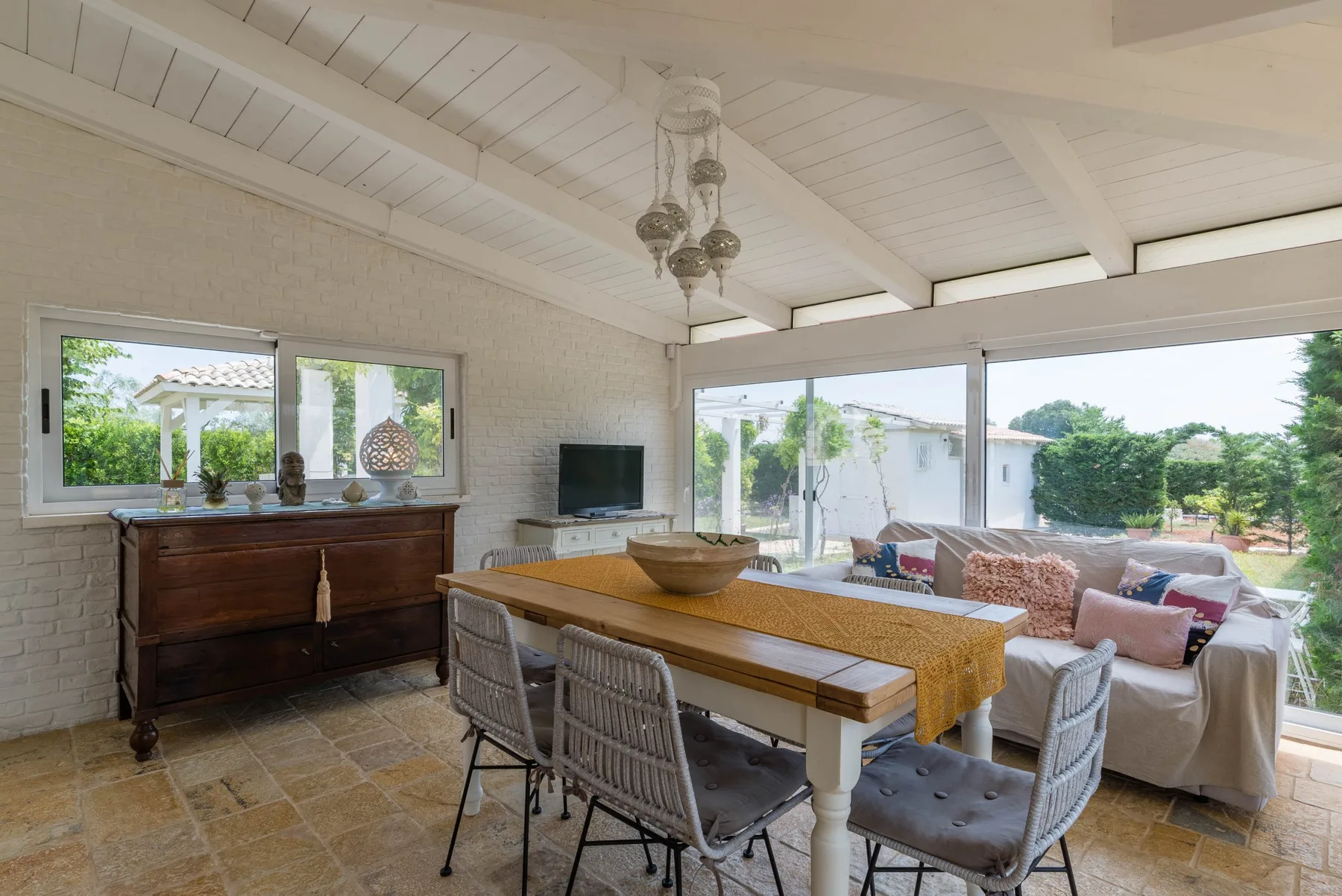 A bright dining and sitting area opens onto a garden through large windows.