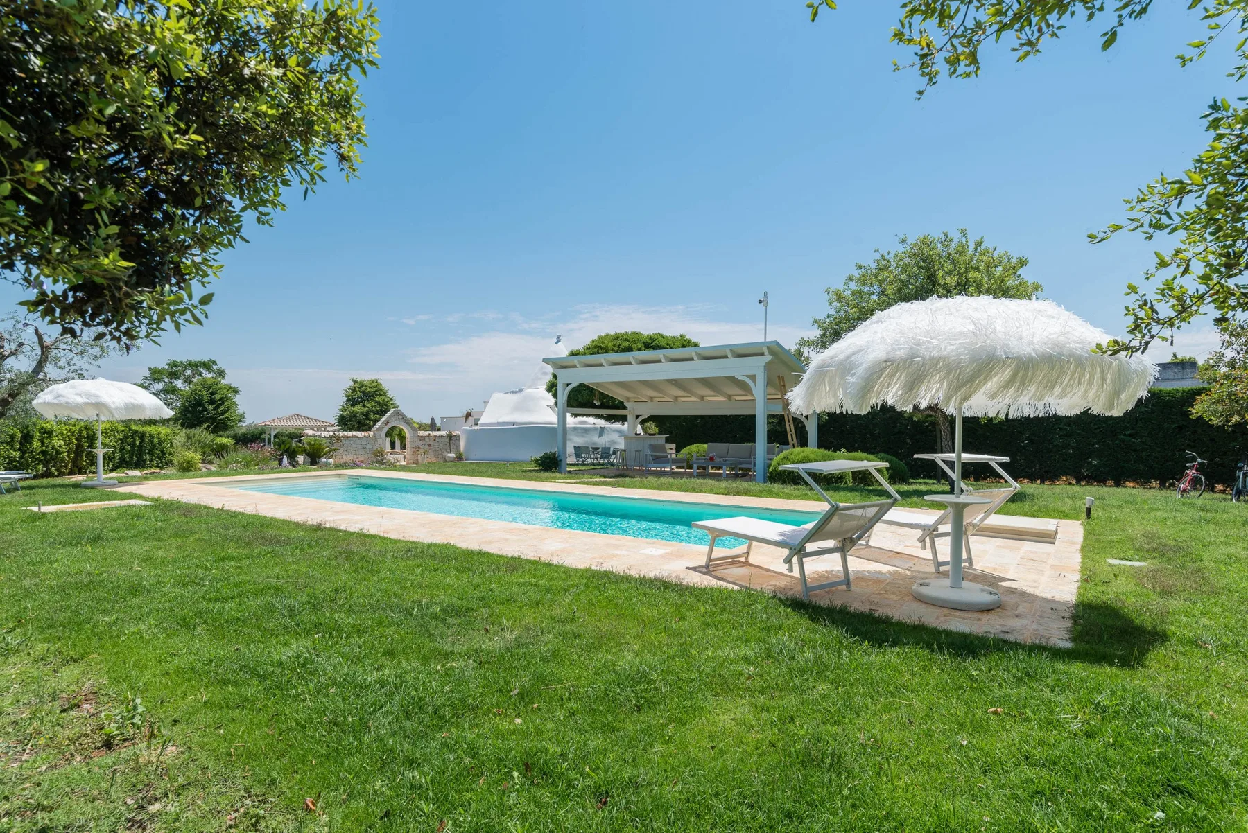 An outdoor swimming pool beside a grassy lawn, shaded by parasols.