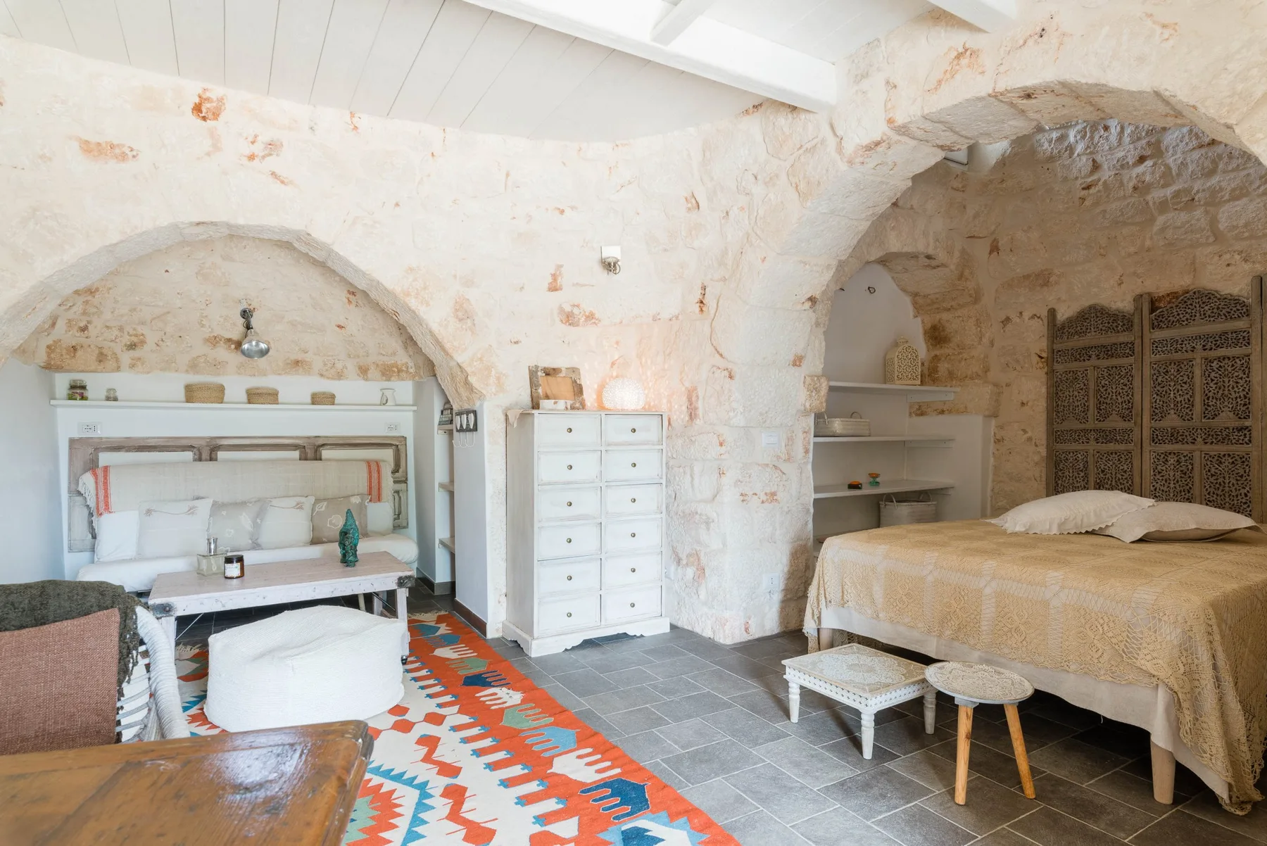 A bedroom with a bed, a desk, and a colorful patterned rug.