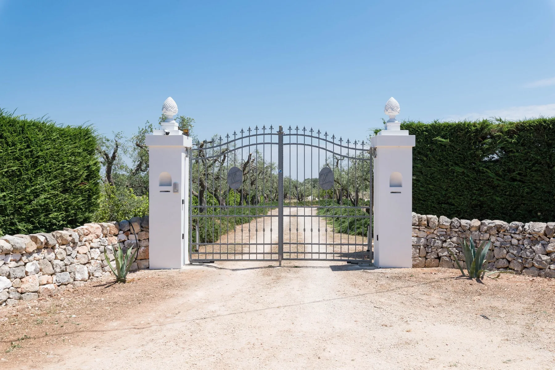 A gated entrance sits between stone walls and trimmed hedges.