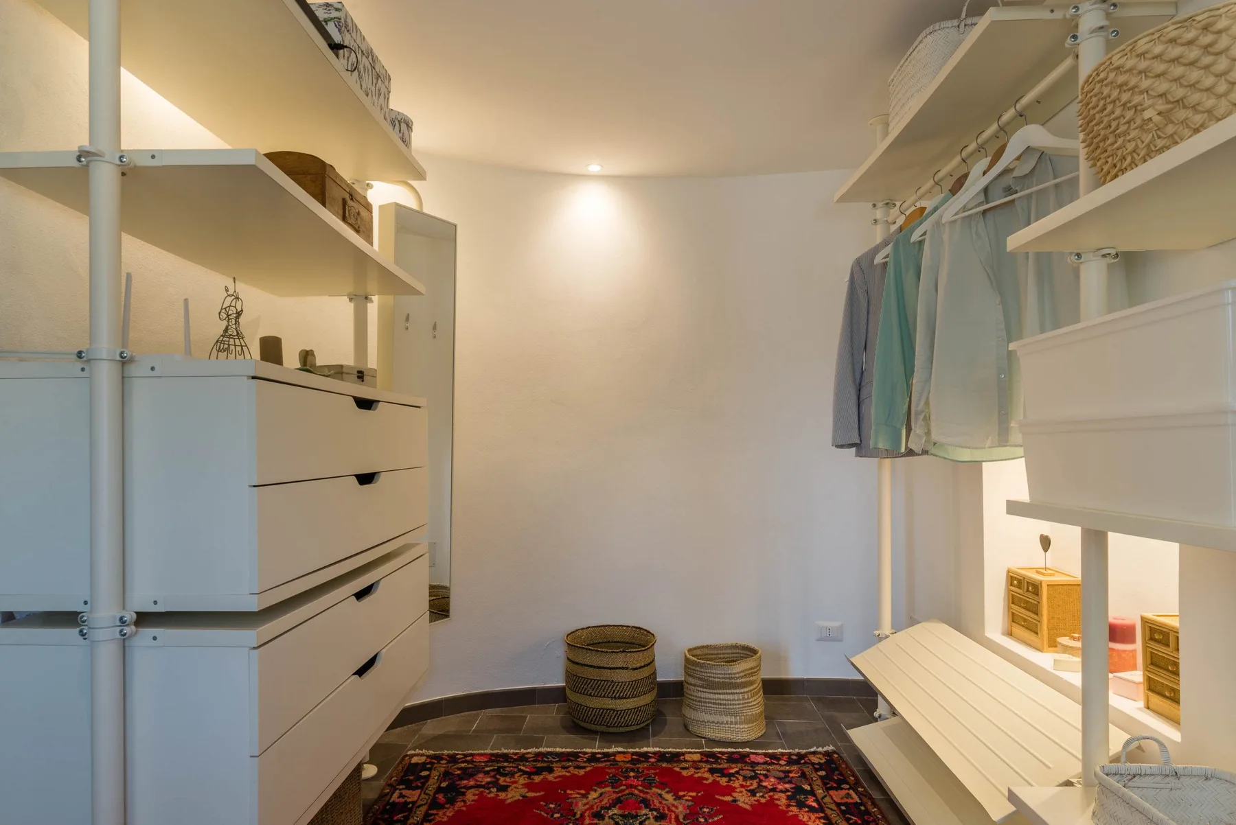 A walk-in closet with hanging clothes, built-in drawers, and a patterned rug.