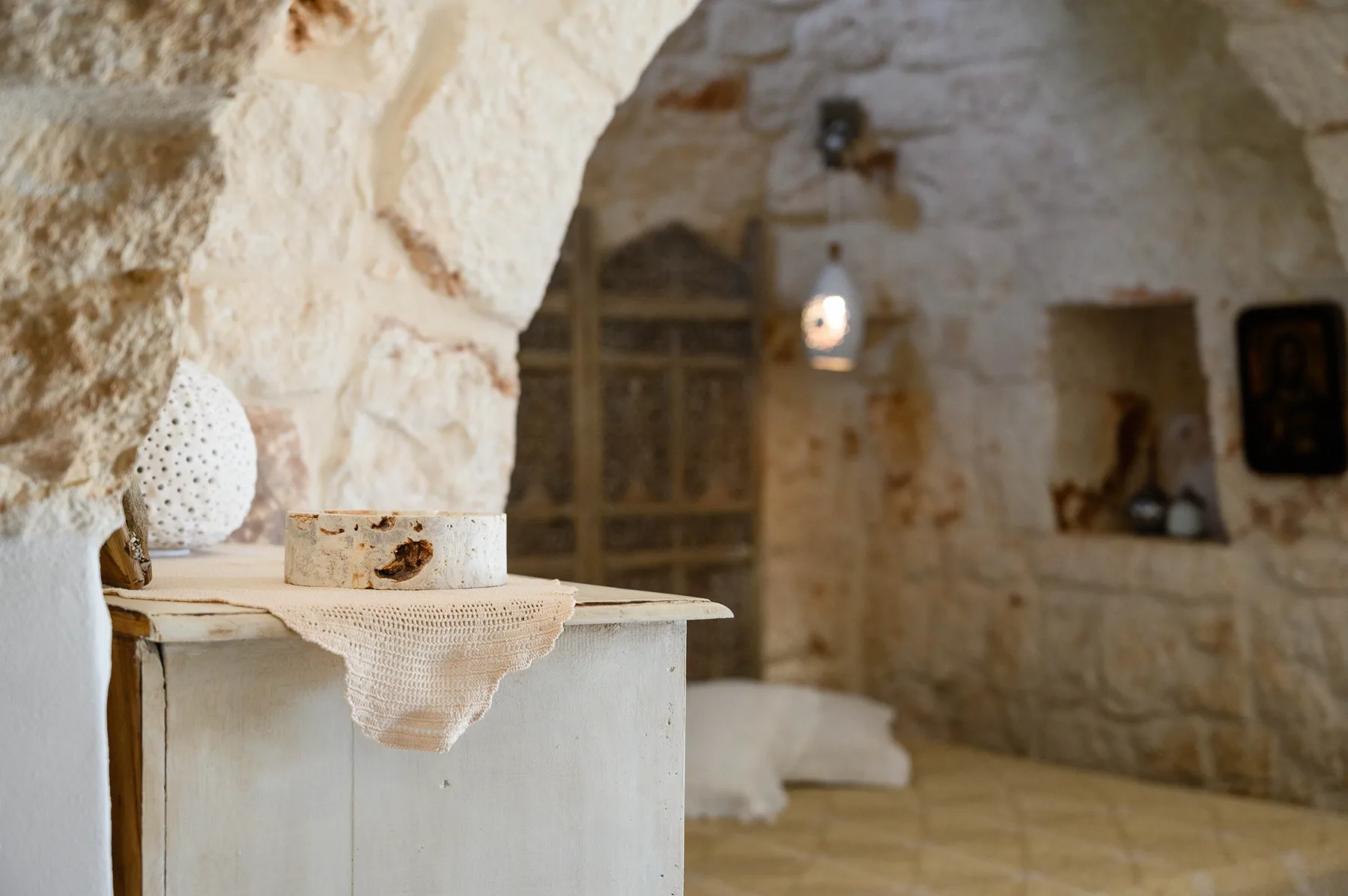 A stone bedroom with an arched ceiling, a bed, and a small bedside table.