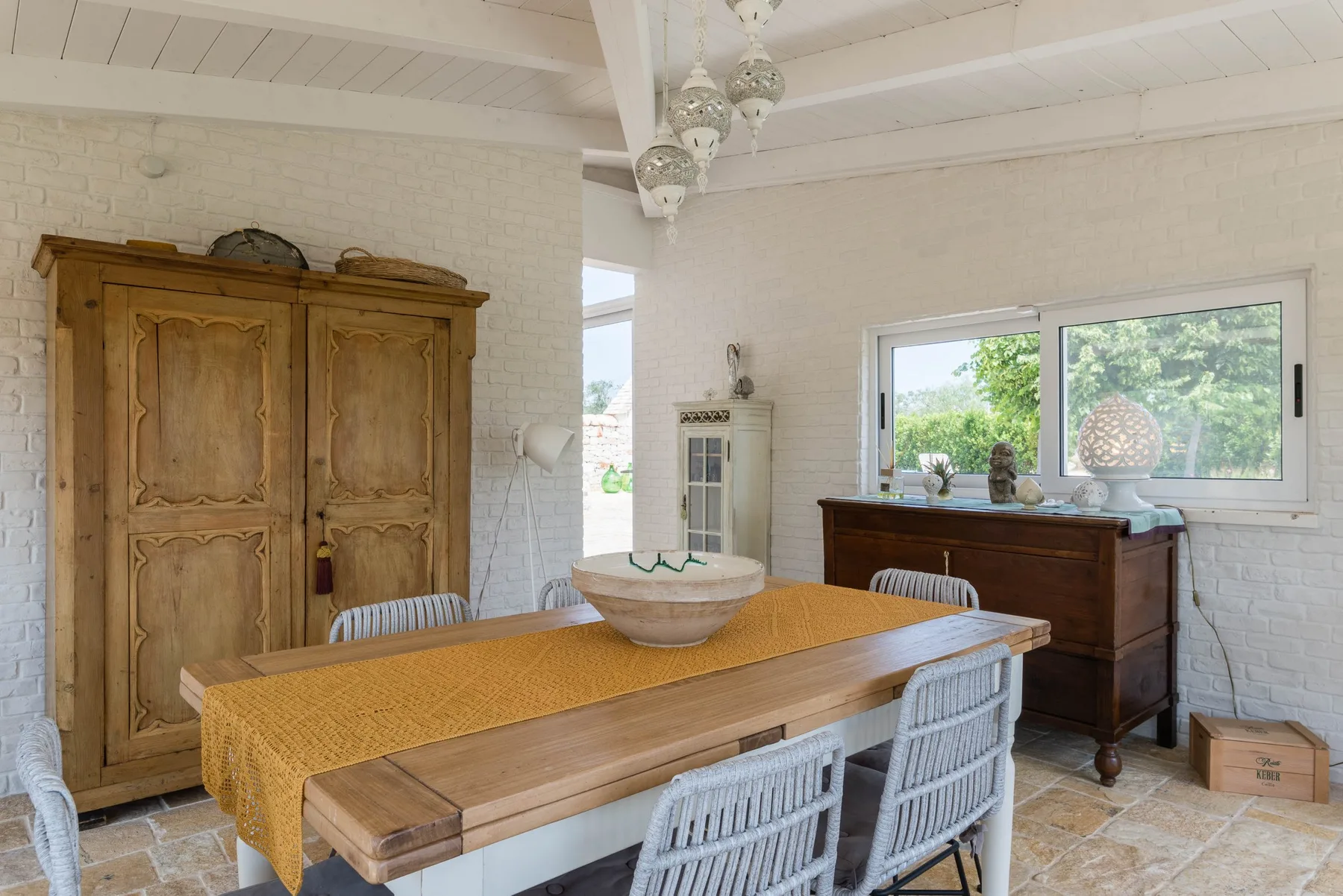A bright dining room with a long wooden table and chairs beneath hanging lights.