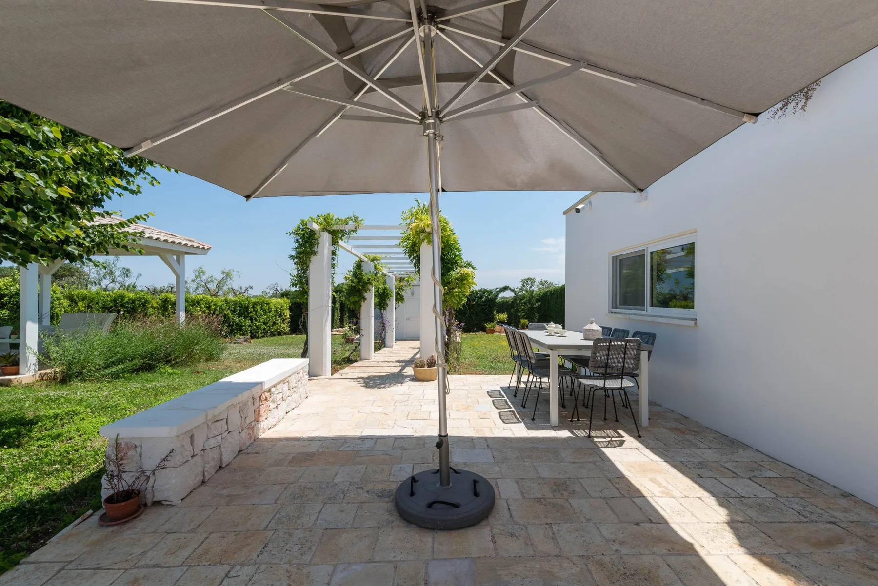 A sunny stone patio with a large umbrella and outdoor dining table.