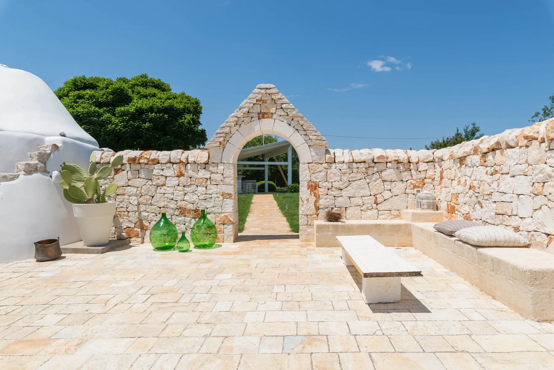 A sunlit stone courtyard with an arched gateway and built-in seating.